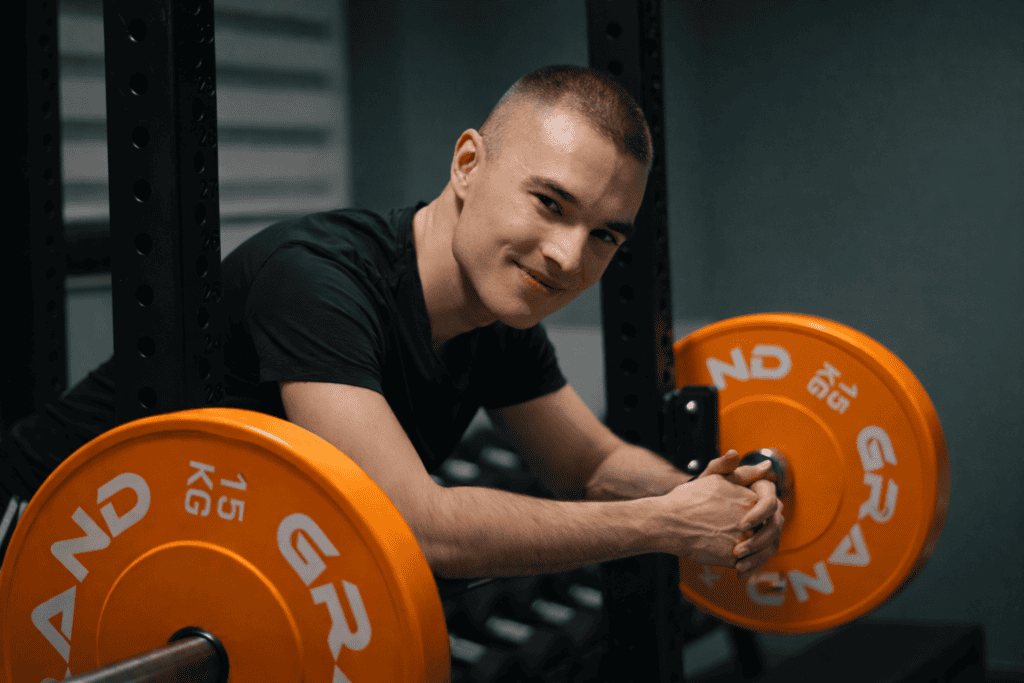 Mężczyzna w siłowni oparty o sztangę z obciążeniem 15 kg. Trening siłowy.